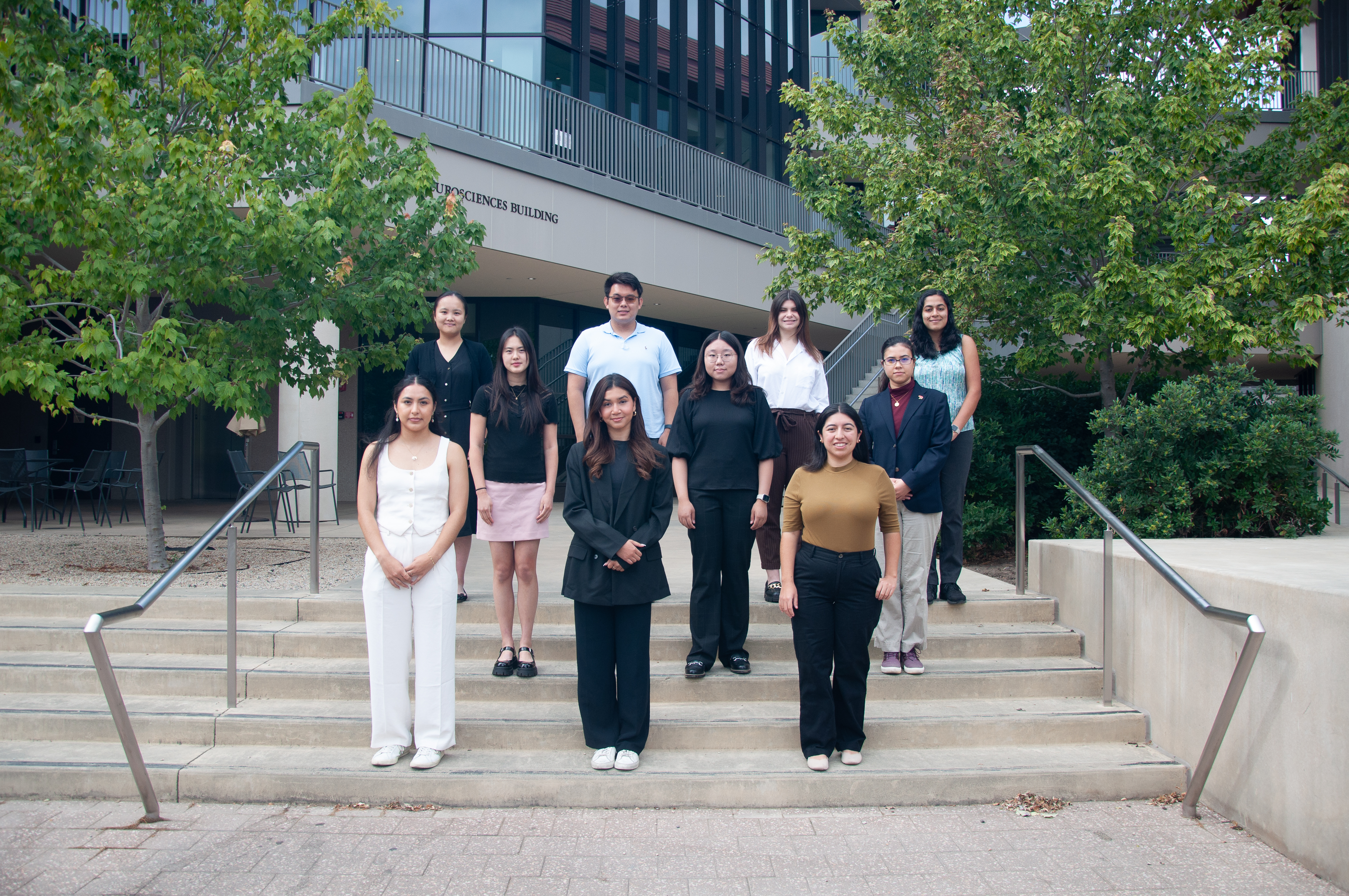 The 2024 NeURO cohort stands on the steps outside the Wu Tsai Neurosciences Building, posing for a photo. They are arranged in rows, with some standing on the steps and others at the base.