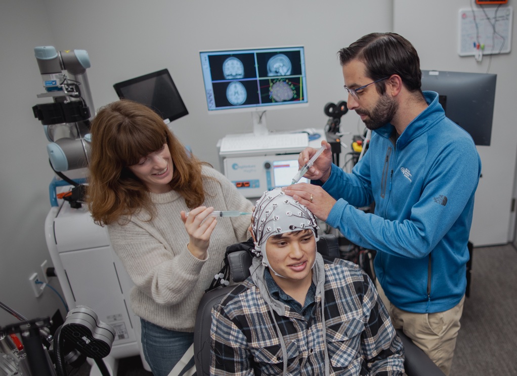 Corey Keller and Milena Kaestner work to prepare a research subject for simultaneous EEG recording and TMS brain stimulation in the Koret Human Neurosciences Community Laboratory at the Wu Tsai Neurosciences Institute.