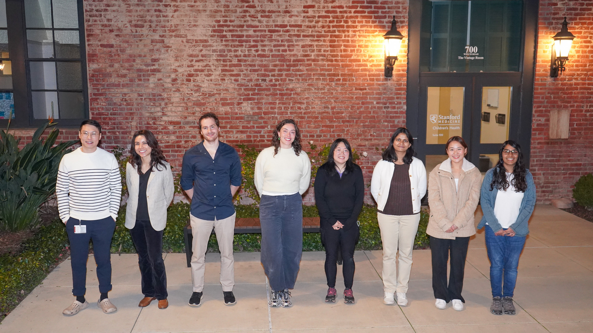 Seven people pose for a photograph in front of a brick wall.