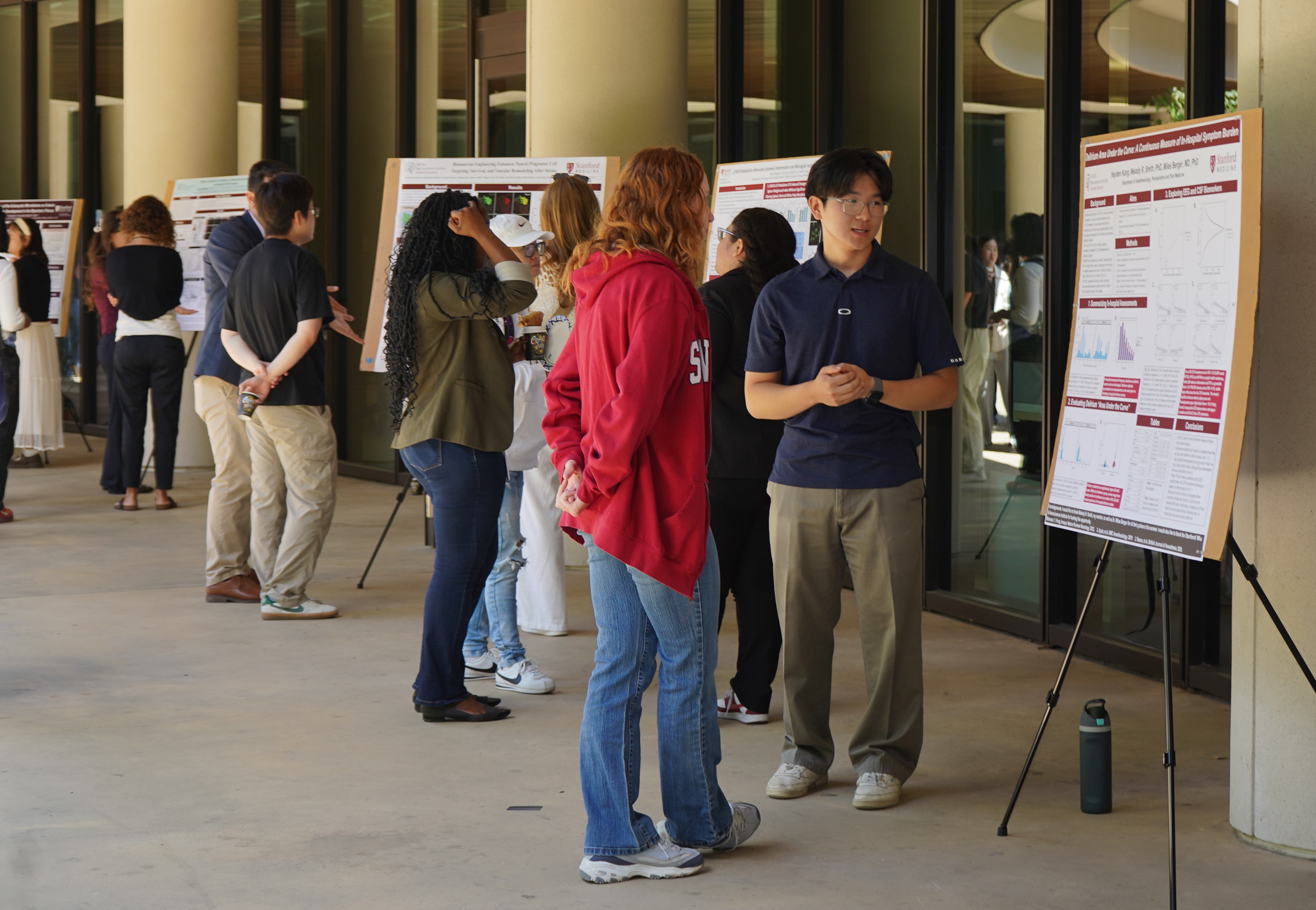Student present research posters to a crowd in a courtyard.