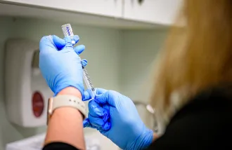 A person wearing blue gloves prepares a vaccine shot.