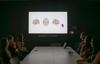 Laura Gwilliams, Jill Kries, and other members of the Gwilliams lab sit around a table discussing research presentation.