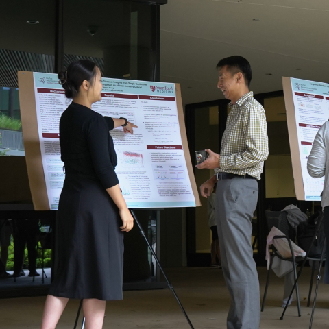 A researcher presents her poster to a director at the 2024 NeURO/NeURO-CC poster session, with detailed charts and graphs displayed on the poster board.