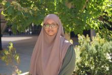 Ladan Abdi stands in front of green foliage and looks to the camera