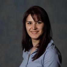 A professional headshot of Shaghayegh Navabpour wearing a button up shirt against a grey background.