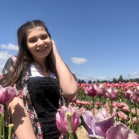 Picture of Liv. In the picture, she is in a field of flowers looking at the camera smiling.  