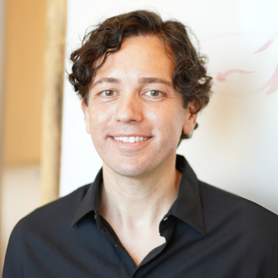 Zachary Knight smiles at the camera and is wearing a black button-up collared shirt, standing inside in front of a light background.