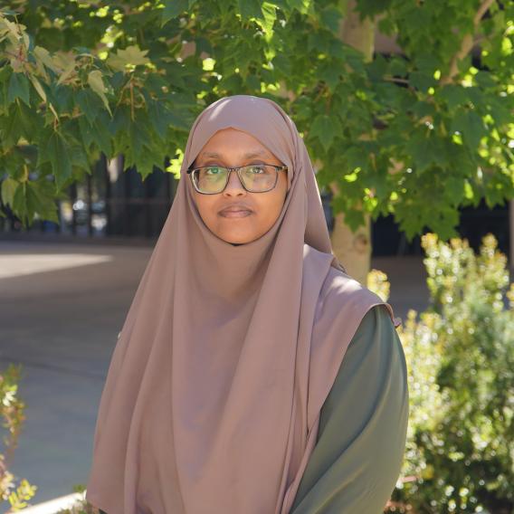 Ladan Abdi stands in front of green foliage and looks to the camera