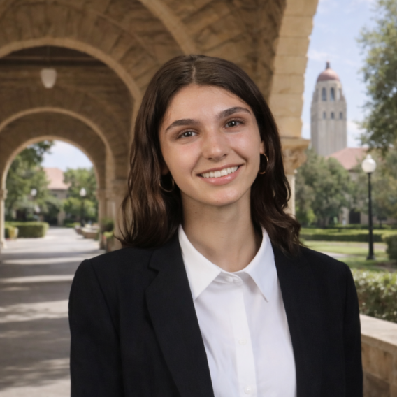 Hannah Saab wearing a black blazer and white collared shirt standing in Stanford sandstone archway with Hoover Tower visible in the background.