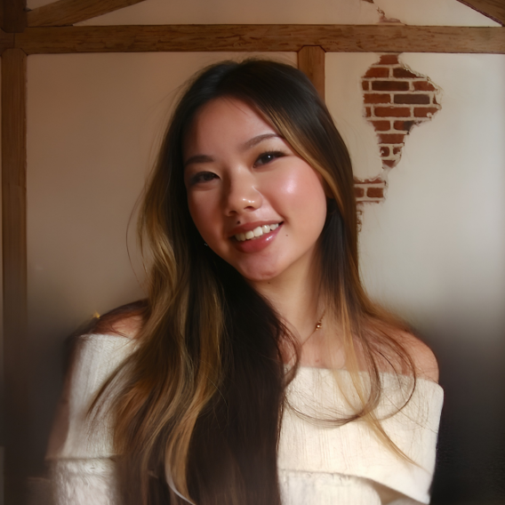 Head-and-shoulders portrait of a person with long brown hair and blonde highlights wearing an off-shoulder cream top and thin gold necklace, posed against a wall with exposed brick and wooden beams.