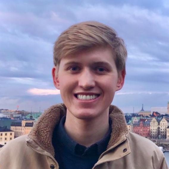 Chase smiles at the camera in front of a cloudy-sky background