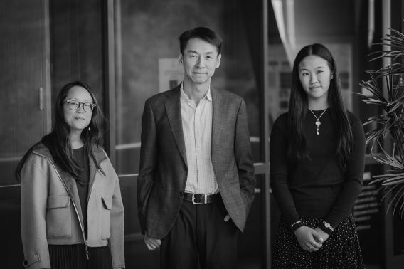 Colette Guey-Chi Chen, Kang Shen, and Peggy Guey-Chi Chen stand together outside a building, facing the camera. The photo is black and white, and all three appear calm and composed.