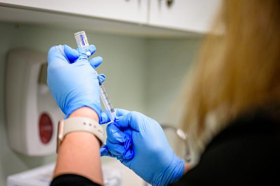 A person wearing blue gloves prepares a vaccine shot.