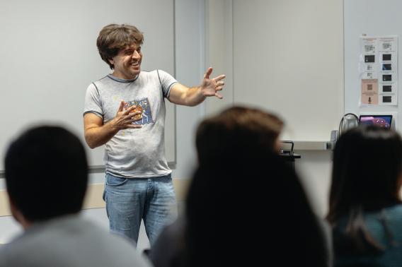 Karl Deisseroth smiles and gestures toward others seated in front of him.